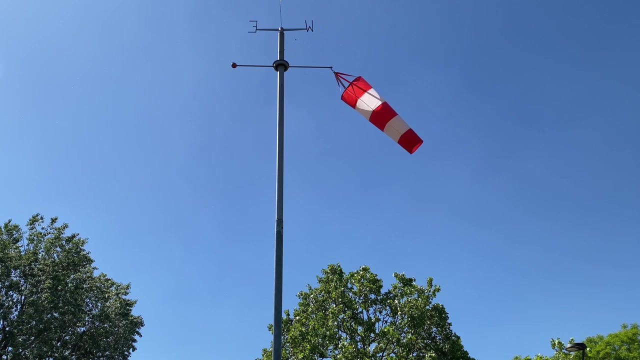 Rød og hvid vindpose blæser i vinden mod en klar blå himmel. Lufthavnens vindstrømpe med vindfløjindikator, der viser vindretning og -hastighed. 4K.