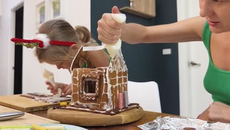 mom and daughter decorating a gingerbread house