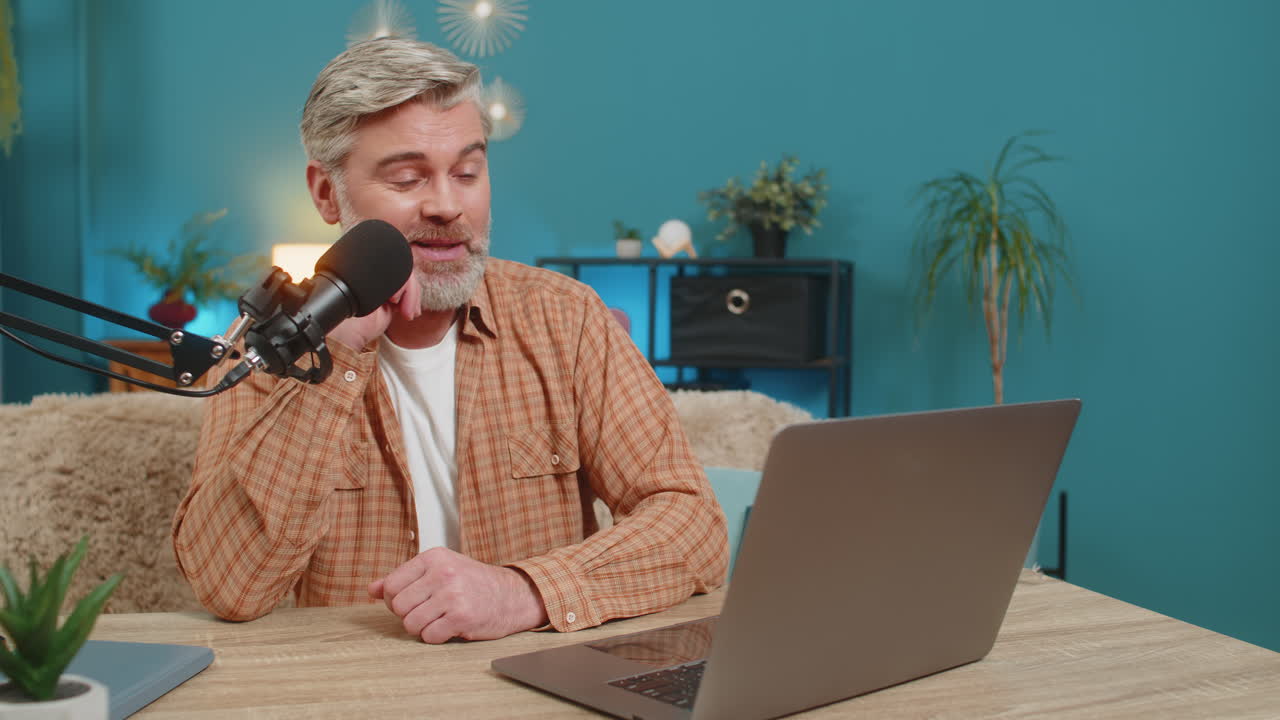 Mature man at home table speaking into microphone during live online stream responding with energy