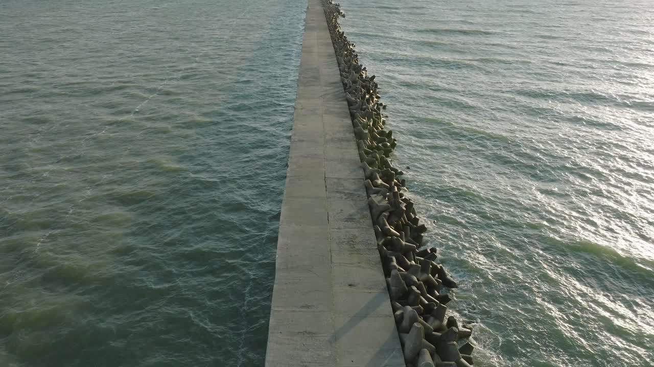 vista aérea del muelle de concreto del puerto de liepaja, costa del mar báltico, tarde soleada de verano, luz de la hora dorada, grandes olas salpicando, amplio disparo de drones avanzando
