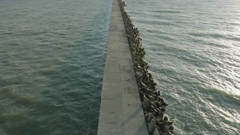 aerial establishing view of port of liepaja concrete pier, baltic sea coastline , sunny day summer evening, golden hour light, big waves splashing, wide drone shot moving forward