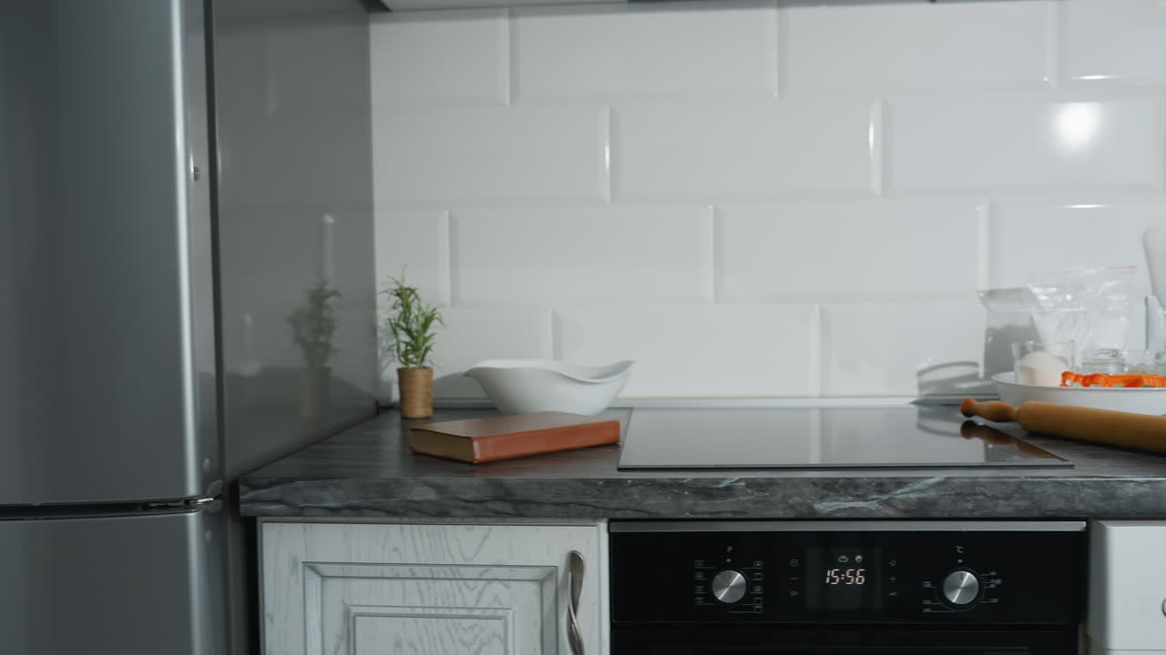 Cucina moderna ed elegante con frigorifero in acciaio inossidabile, piano di lavoro in marmo nero e mobili bianchi, libro ordinato, pianta decorativa e utensili da cucina