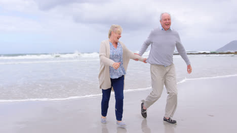 front view of old caucasian senior couple running on the beach 4k