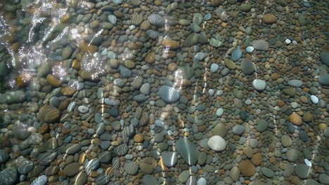 smooth pebbles under clear water with sunlight reflections