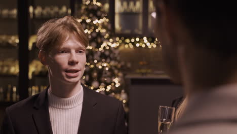 Close-Up-View-Of-Red-Haired-Man-Wearing-Stylish-Clothes-While-Talking-And-Holding-Champagne-Glasses-At-New-Year's-Party-1