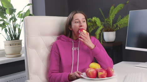 Young-Woman-Sitting-At-Desk-And-Eating-A-Red-Apple-1
