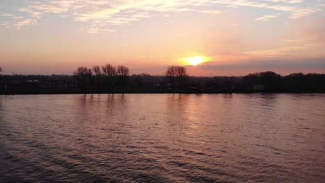 Antena-Sobre-El-Cielo-Naranja-Del-Atardecer-Reflejado-En-Oude-Maas-En-Puttershoek-Con-Dolly-Justo-Pasando-La-Boya-Flotante