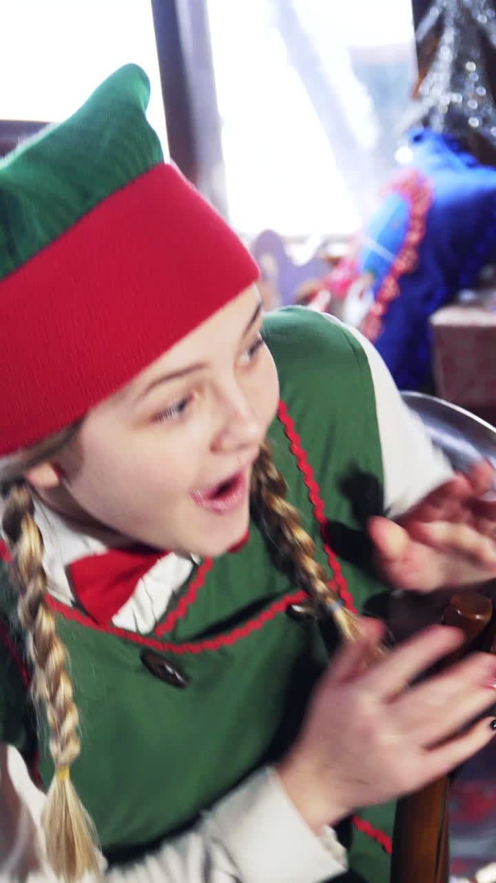 Excited elf sitting at the table. Joyful female in elf green costume is looking at something with surprise. Vertical video