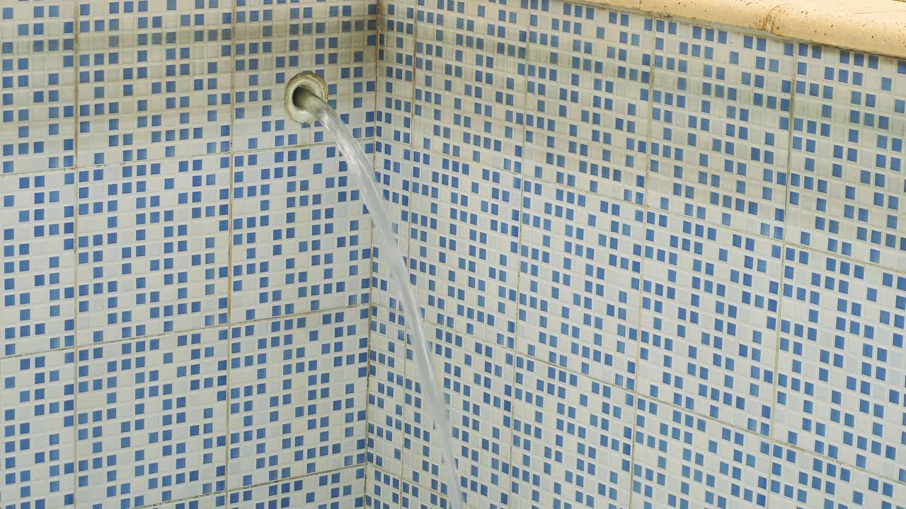 A water jet pours from a tube, filling a tiled swimming pool