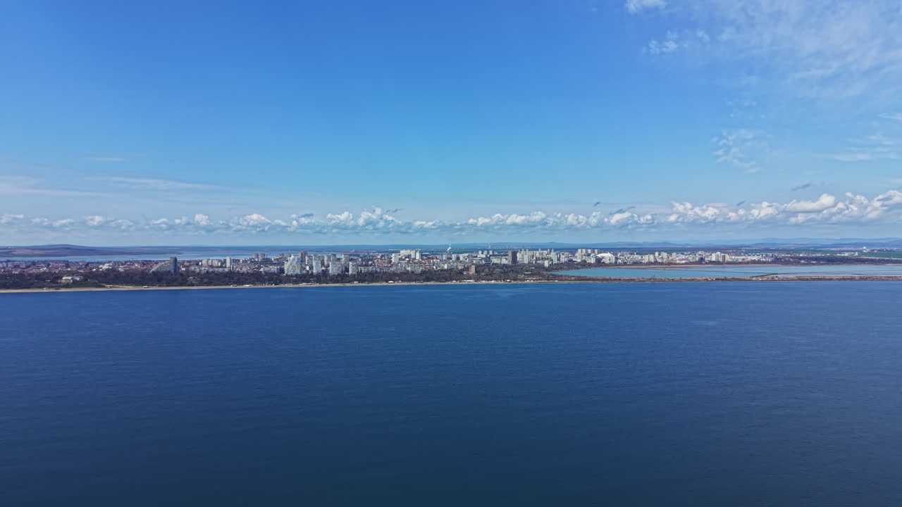 Wide view of coastline with city skyline near the water during daytime under a clear blue sky with some clouds in the distance
