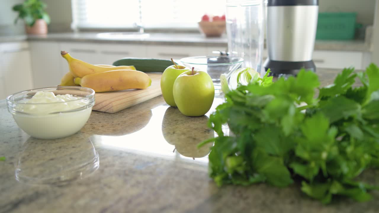 Camera pulling back is revealing herbs while apples are moving toward blender for smoothie prep