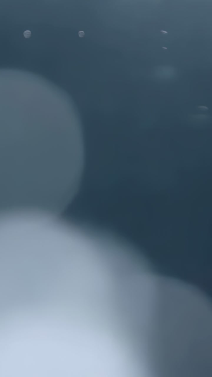 Vertical video: Frames shifting bluish bokeh circles drifting on dark gray backdrop with specks