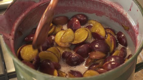 cooking and stirring homemade plum jam in preserving pot using wooden spoon