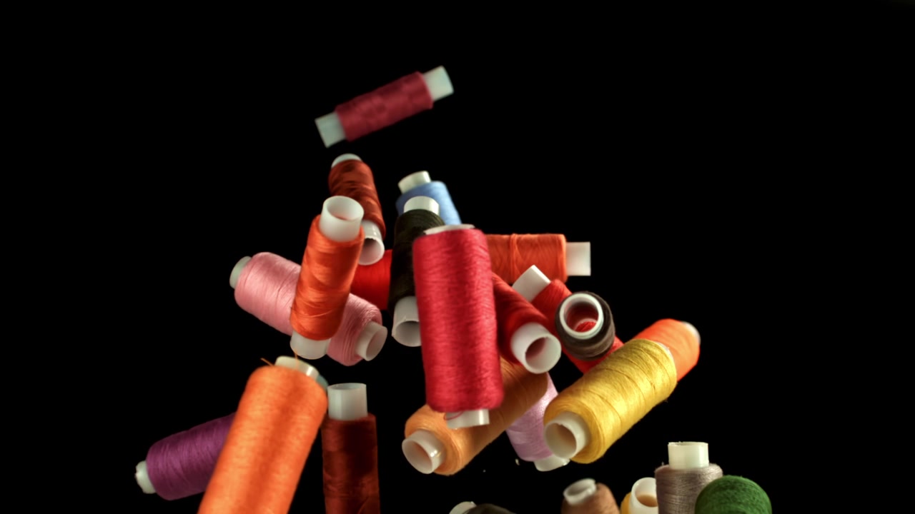 Colorful Spools of Thread Falling in Slow Motion on Black Background
