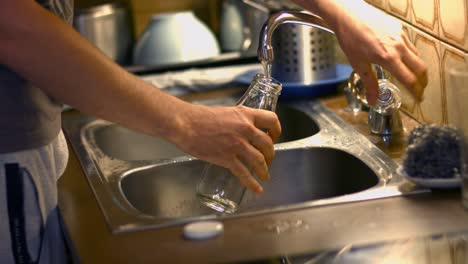 close up of a person filling a glass bottle with fresh drinking water from a tap