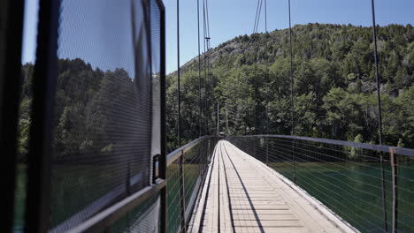 a suspension bridge crosses a turquoise river, surrounded by lush green forest