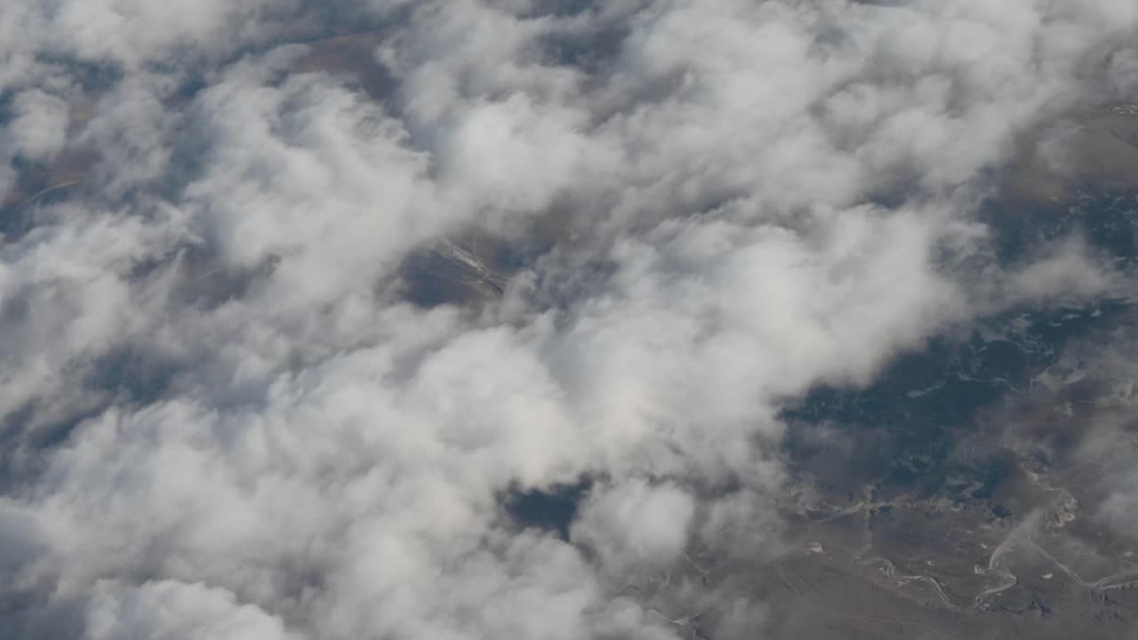 Aerial drone view flying above thick clouds with terrain faintly visible below, capturing a dreamy sky-atmosphere transition