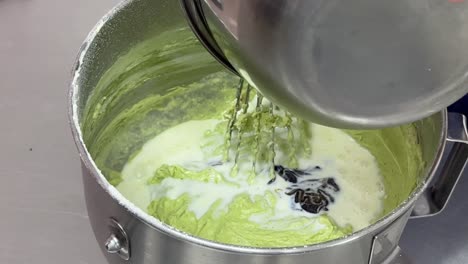 pastry chef hand mixing with a whisk, patiently mixing matcha flavor cake mixture, slowly adding milk and vanilla essence into the bowl, close up shot