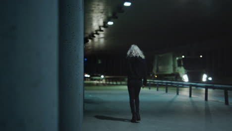 Woman-walking-away-tunnel-with-driving-cars-at-night-city-highway.