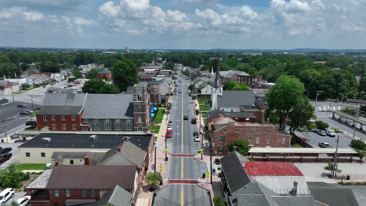 Quaint small American town with cars on street and church on junction. Aerial wide shot. Sunny day in summer. Historic buildings and homes in village