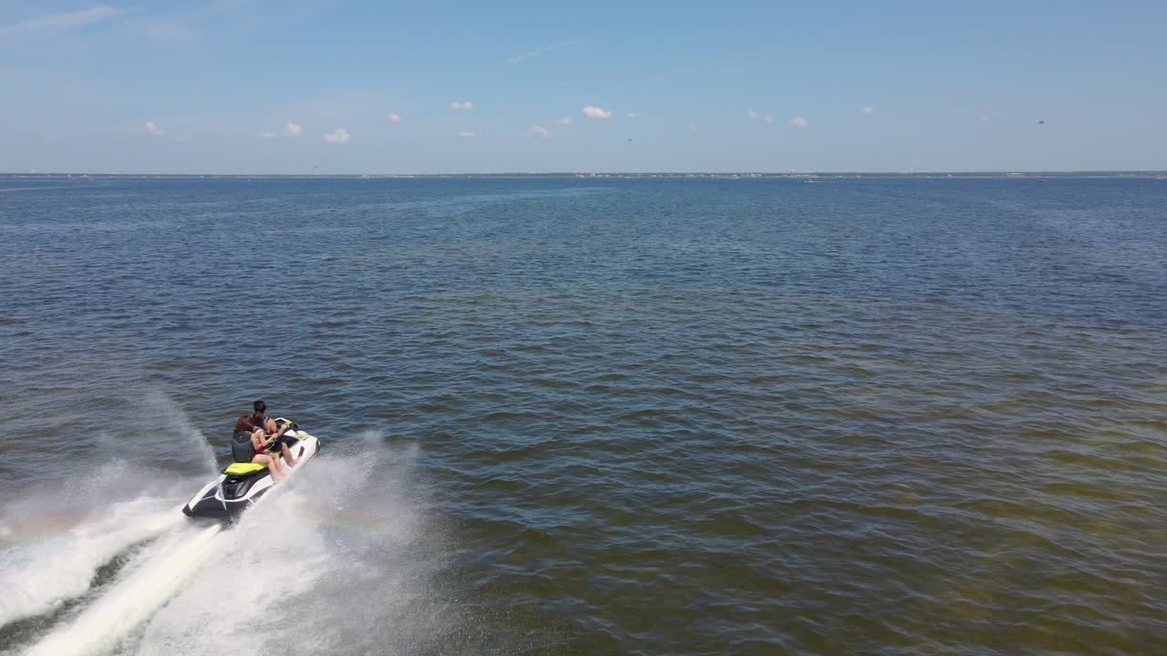 disparo aéreo de una pareja de paseos en jet ski rebotando a través del océano abierto agua azul verde disfrutando del día