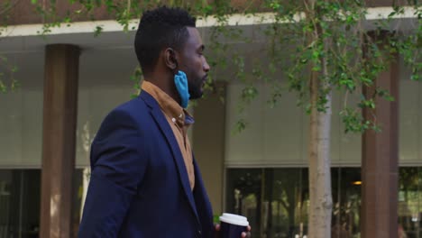 african american businessman with face mask walking in city street