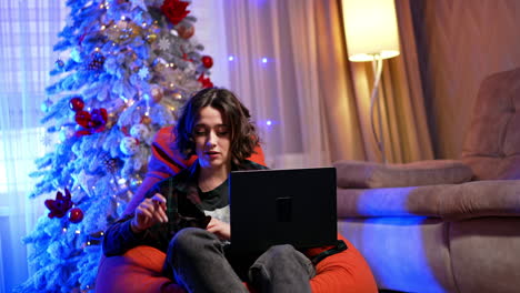 boy on laptop during holidays. a young boy sits comfortably on a red bean bag, focused on his laptop, surrounded by festive decorations