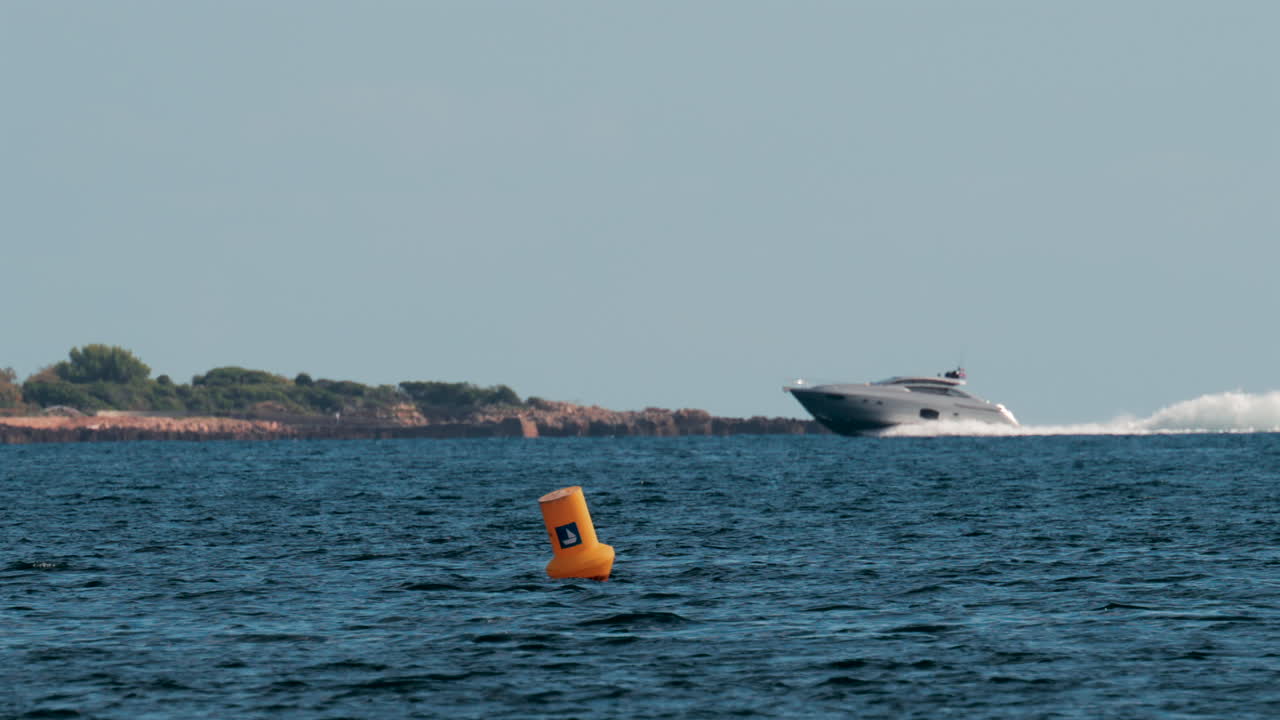 A fast moving yacht glides past a luxury coastal villa surrounded by trees and clear blue water