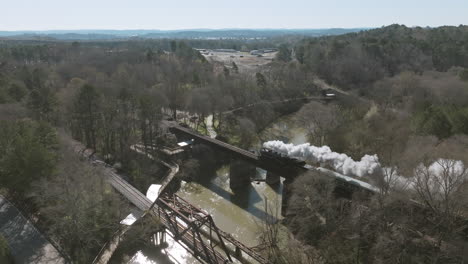 Slow-motion-wide-aerial-drone-shot-of-a-steam-train-engine-moving-across-a-bridge-in-Chattanooga,-TN