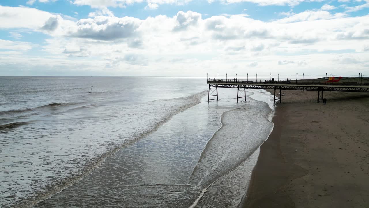 típico balneario inglés, fotografiado con un dron volando hacia el sol dando un punto de vista aéreo con una amplia extensión de playa con un muelle y olas rompientes-1