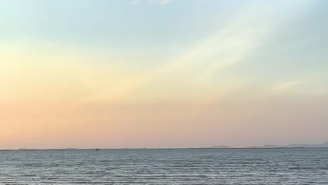 a tranquil scene of a pastel-colored sunset with a boat silhouette on the horizon.