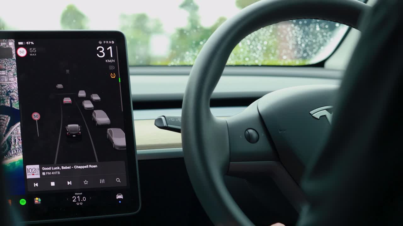 Driver maneuvers electric car using steering wheel and dashboard screen alerts. Bright, rainy environment with focus on safety features