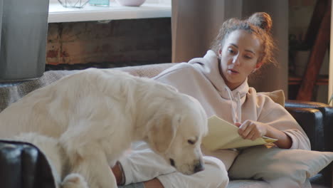 woman relaxing on couch with dog and reading a book