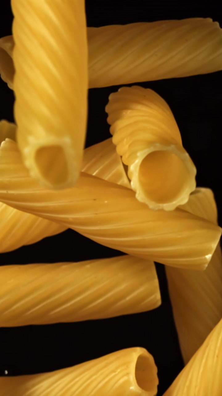 Primo piano di pasta rigatoni secca che cade su sfondo nero