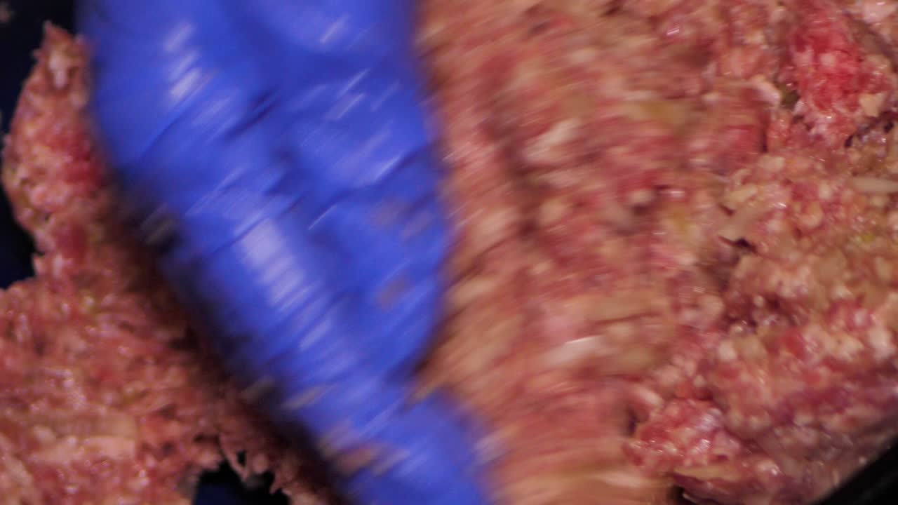 impastare a mano la carne macinata con le cipolle in guanti blu