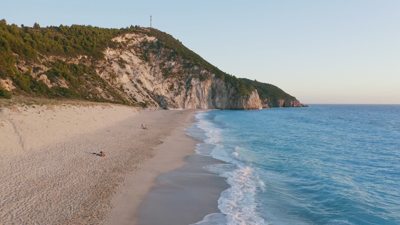 низкий взгляд с воздуха на прекрасный пляж милос в лефкаде, ионический остров, греция. закат золотой солнечный свет и чистые волны ломают бирюзово-голубое море на берегу