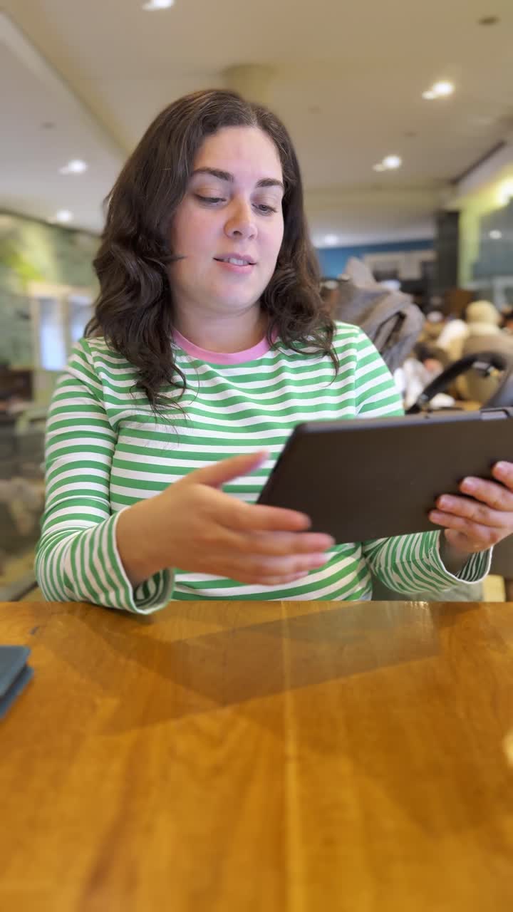 Young adult woman using a tablet in a coffee shop, choosing from a digital menu