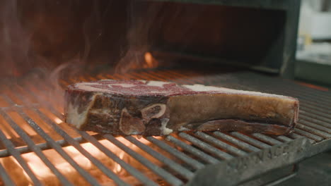 la mano del chef deja caer una gran rebanada de carne de res seca australiana en una parrilla de metal con fuego y llamas