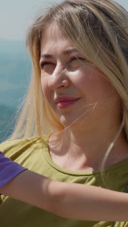 adorable little girl hugs smiling mother standing on ground near aerial lift against misty distant mountains on sunny day closeup slow motion