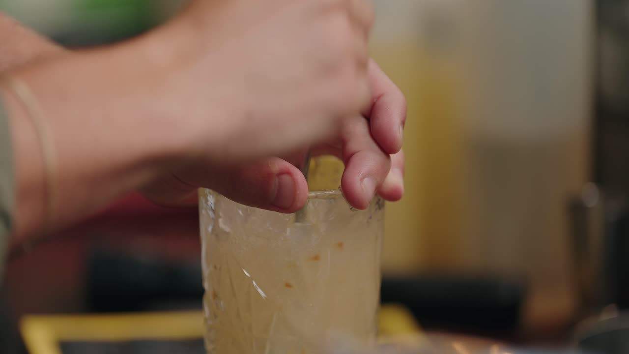 closeup of hands mixing cocktail with ice in transparent textured glass