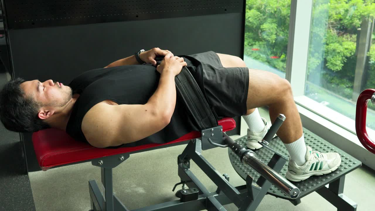 Athletic man doing barbell hip thrusts on a bench in a sunny Bangkok gym interior
