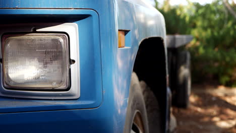 slide right along the headlight and side of an old vintage blue cargo truck with tires parked on a dirt lot