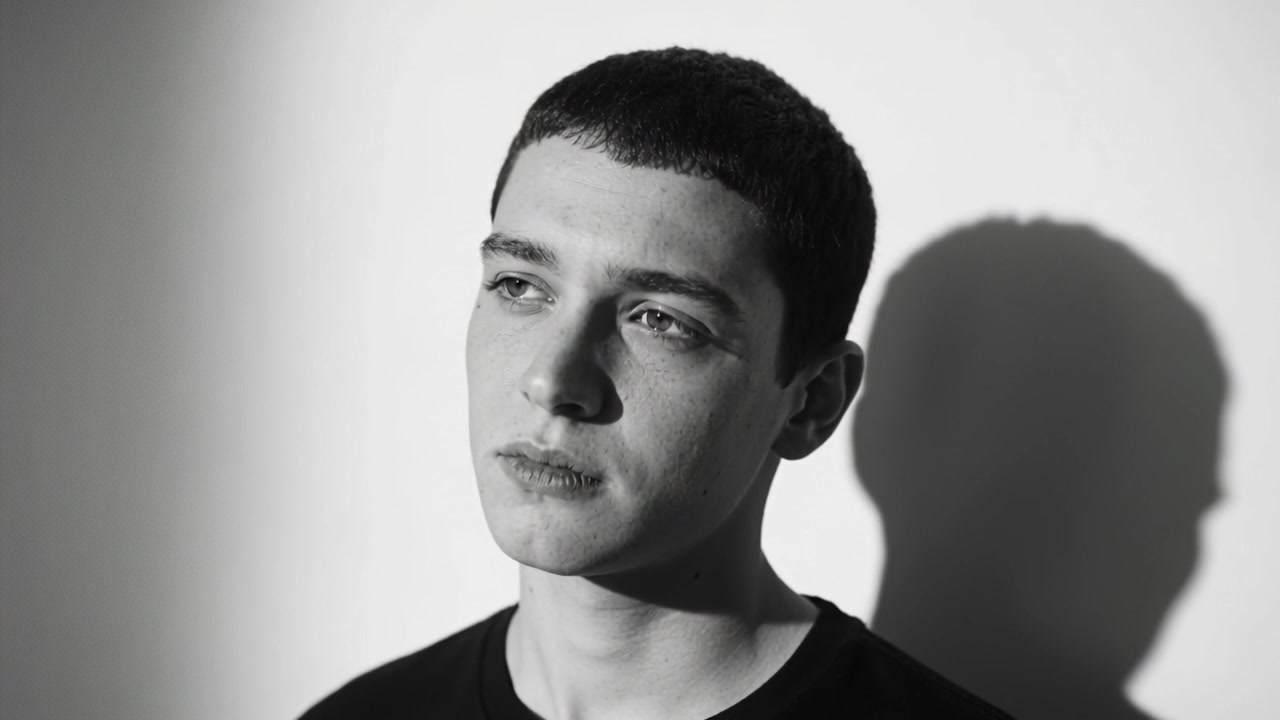 Shifting man responding to camera start, moving gaze and tilting head in studio, with wall shadow
