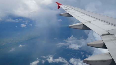 4k footage. flight over the rainbow. aerial view through an airplane window. wing airplane and beautiful white clouds in blue sky for travel background. traveling by air