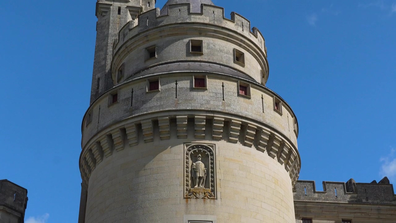 Veduta dal basso di un'imponente torre rotonda al Château de Pierrefonds con merlature, tetto conico, muratura e dettagli difensivi medievali