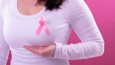 Video-of-midsection-of-caucasian-woman-wearing-pink-cancer-awareness-ribbon,-with-pink-background