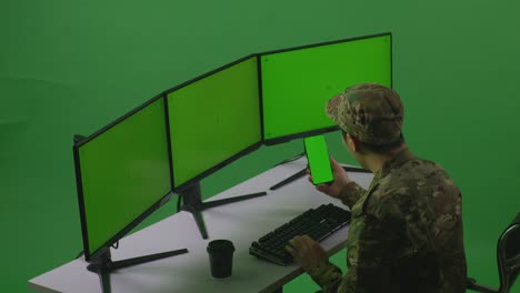 side view of happy asian man soldier looking at mobile phone green screen and celebrating while working with multiple computer monitor in green screen studio