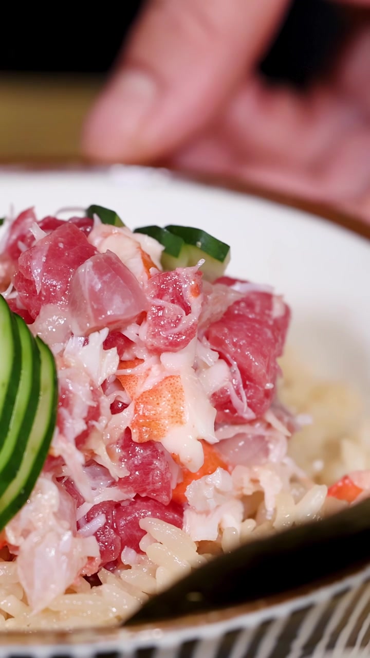 Primo piano di uno chef che posiziona fette di cetriolo su una ciotola di pesce fresco kani don