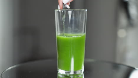 spoon stirring bright green vegetable juice in a clear glass with a blurred background