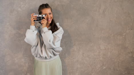 mujer con cámara vintage frente a una pared de hormigón